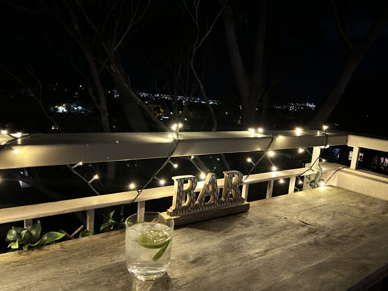 Gin and tonic on a balcony table with fairy lights and city lights in the distance.