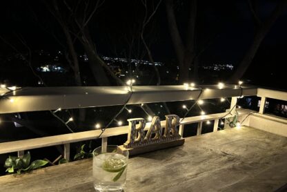 Gin and tonic on a balcony table with fairy lights and city lights in the distance.